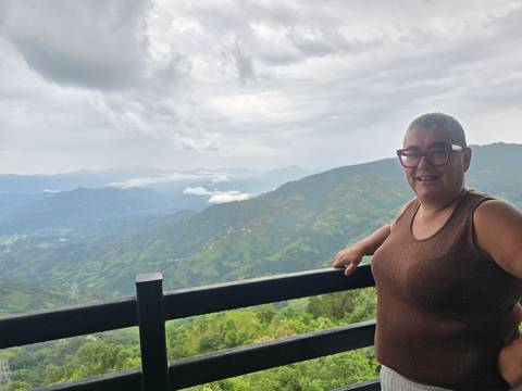Woman smiles at a misty mountain panorama from a wooden balcony viewpoint.