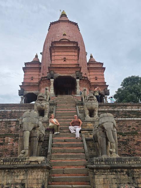Visitors climb and sit on stone steps leading to a brick pagoda temple guarded by stone lions.