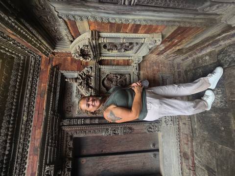 Female traveller poses beside intricate brick and wood carvings on an ancient temple wall.