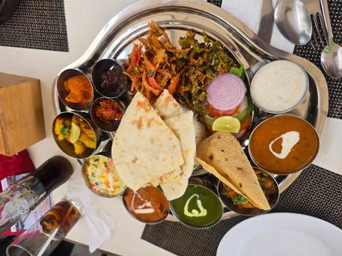 Colorful Nepali thali platter displaying assorted curries, naan, pickles and sides on a metal tray.
