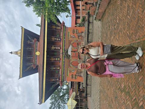 Two women smile in front of a multi-tiered pagoda-style temple in a brick courtyard.