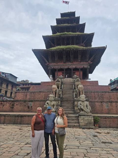 Travellers sit on a wide stone staircase flanked by statues leading up to an ancient pagoda temple.