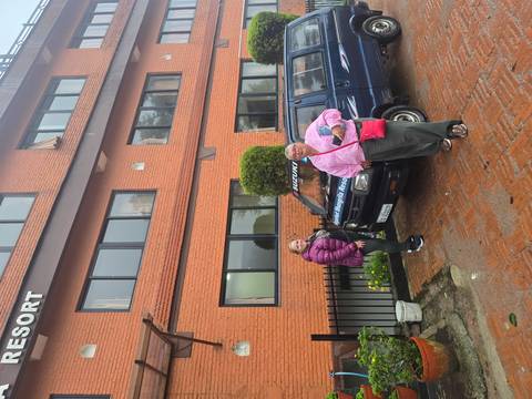 Two women stand beside a blue Suzuki minivan outside a brick resort building on a wet day.