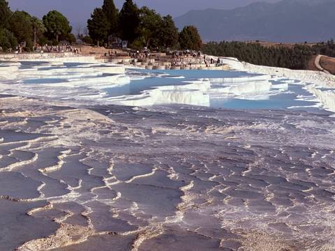 white travertine terraces of Pamukkale with shallow turquoise pools and visitors walking