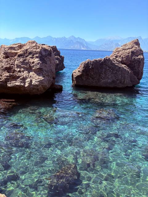 Crystal-clear turquoise sea water glistening around large coastal rocks.