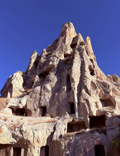 A towering honey-colored rock formation carved with ancient cave dwellings against a clear blue sky.