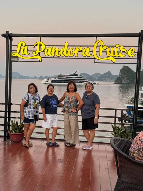Four women posing on a boat deck with a luxury cruise ship and limestone karsts in the background.