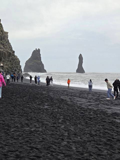 Visitors scatter along the black sands of Reynisfjara beach with dramatic sea stacks rising from the surf.