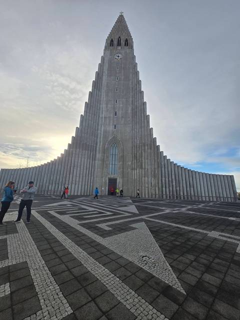 Modernist concrete facade of Hallgrimskirkja soaring into a bright Reykjavik sky with visitors at entrance.