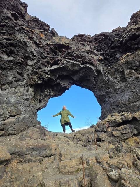Traveller poses triumphantly beneath a natural lava arch against a vivid blue Icelandic sky.
