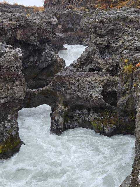 Eroded volcanic rock formations rise amid whitewater rapids carving through a rugged canyon.