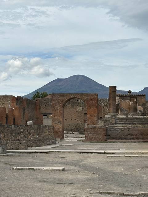 Ancient brick arches and columns of Pompeii with Mount Vesuvius looming in the background.