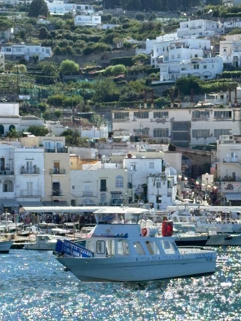 Busy waterfront town with pastel buildings and ferry docks on a hazy Mediterranean morning.