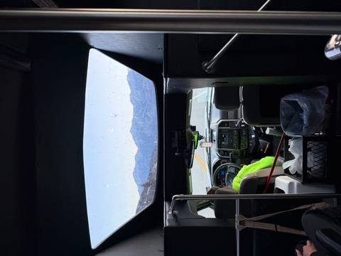 Interior of a tour bus looking through the front windshield toward a mountain highway.