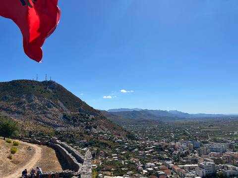 Albanian flag waving above panoramic mountain and valley cityscape.