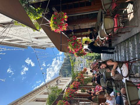 Lively cobblestone alley with hanging flower baskets and outdoor cafés buzzing with people.