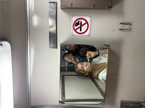 Friends jokingly brush teeth together in a small train washroom mirror.