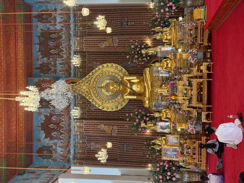 Golden Buddha statues adorn an ornate temple hall where visitors meditate on a red carpet.