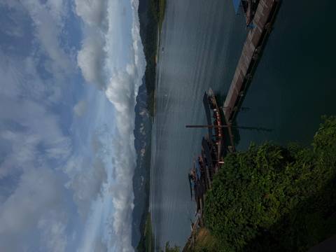 Long-tail boats are moored at a jetty on a broad lake backed by jagged mountains.