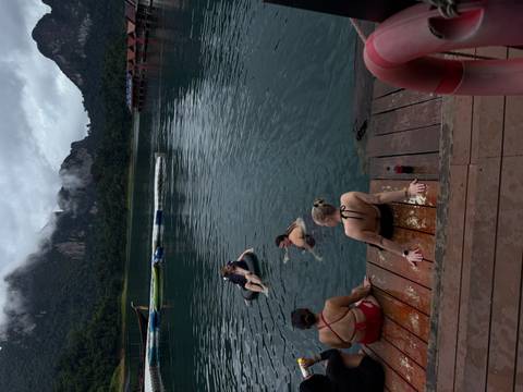 People lounging and swimming off a wooden deck on a tranquil lake set against misty forested peaks.