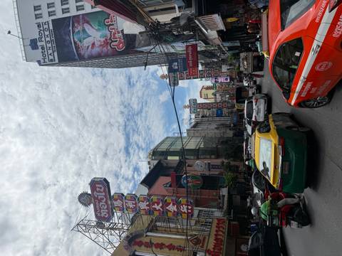 Bustling Bangkok Chinatown street packed with traffic, neon Chinese signs and patchy clouds overhead.
