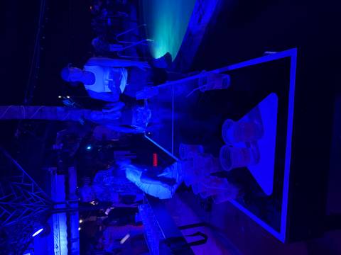 Neon-lit bar scene with travelers playing beer-pong beside a glowing pool during an island party night.