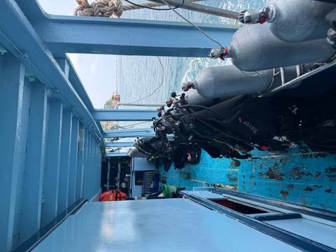 Interior of a dive boat lined with scuba tanks and equipment while cruising on calm sea waters.