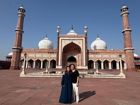 Two travellers posing in front of the grand Jama Masjid courtyard under a cloudless sky.