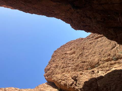 Towering red sandstone canyon walls rise toward a bright blue Moroccan sky.