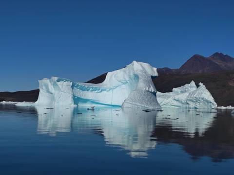 Massive blue-white iceberg floats serenely against rugged mountain backdrop.