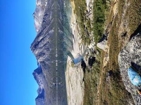 Mirror-like alpine lake reflects rugged peaks and clear blue sky.