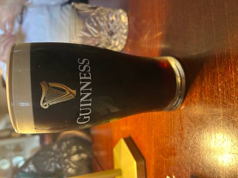 Pint of dark Guinness stout on a wooden pub table with warm interior lighting.