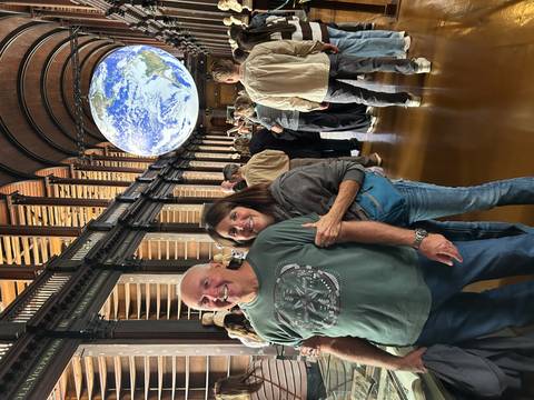 Visitors inside grand vaulted hall with giant suspended globe installation at Trinity College.