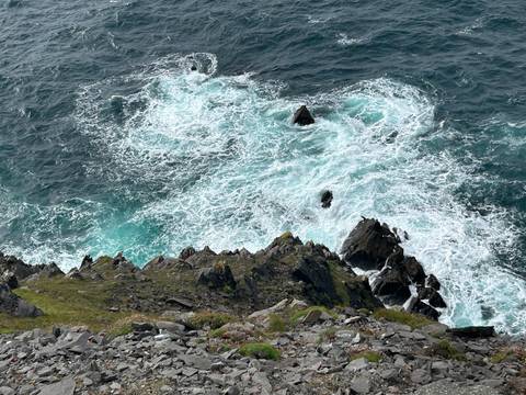 Top view of turquoise surf churning against jagged coastal rocks.