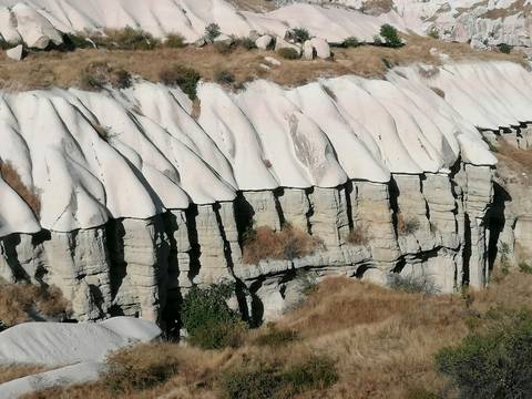 Eroded white-capped rock formations create a rippled cliff face in Cappadocia.