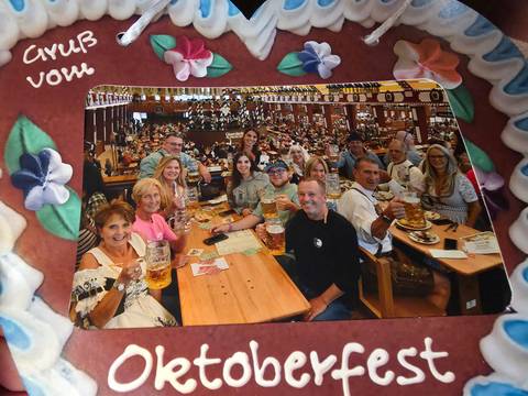 Large group raises beer steins around long wooden tables inside a festive beer hall.