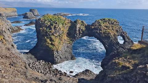 Natural stone arch Gatklettur rises above crashing waves on a rugged coastline.