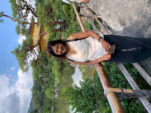 Visitor poses beside the reflective pond of the Golden Pavilion temple.