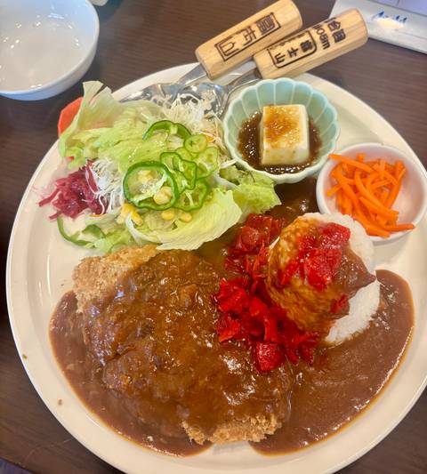 Colourful plate of Japanese curry rice with salad, pickles, tofu, and cutlet.
