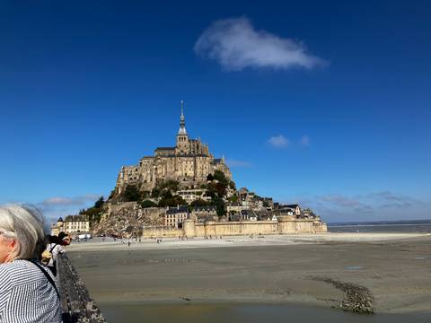 Iconic Mont Saint-Michel rising above vast tidal flats beneath a clear blue sky.