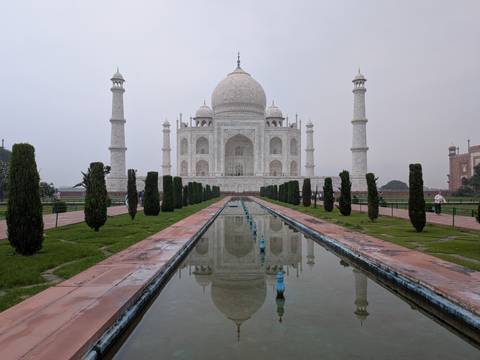 The Taj Mahal and its reflecting pool framed by manicured gardens on a hazy morning.
