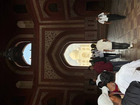 View of the Taj Mahal framed by a Mughal gateway crowded with visitors.