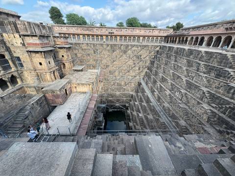 Expansive view into the geometric depths of Chand Baori stepwell with tourists on platforms.