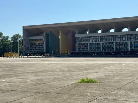 Wide plaza view of Chandigarh’s multicoloured High Court façade with many visitors standing in the shaded arcade.