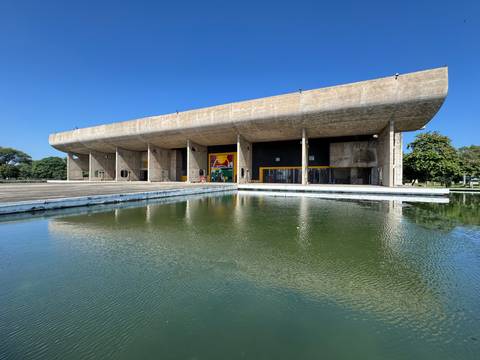 Brutalist cultural building in Chandigarh mirrored in a tranquil water basin under cloudless blue sky.