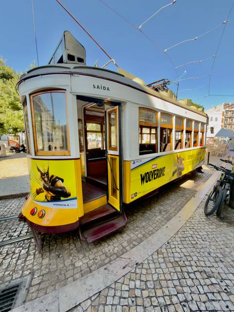 Historic yellow tram advertising Wolverine comics parked at a Lisbon stop.