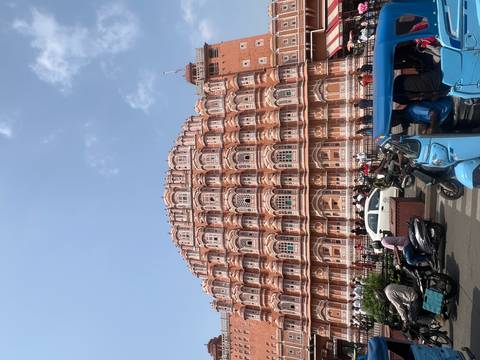 Street-level view of Jaipur’s Hawa Mahal with busy traffic of tuk-tuks and motorbikes in foreground.