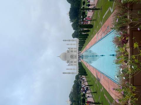 Classic symmetrical view of the Taj Mahal with reflecting pool and trimmed gardens under hazy sky.