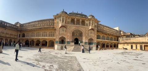 Panoramic courtyard of Amber Fort richly decorated with frescoes and scattered visitors on sunny day.