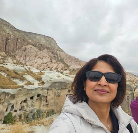 Selfie of traveller wearing sunglasses with Cappadocia’s pink rock formations and cave dwellings behind.